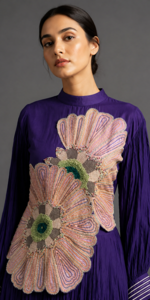 Luxury royal purple Indo-Western dress with oversized blush floral appliqué embroidery, intricate beadwork, full sleeves and flowing crinkled silhouette.
