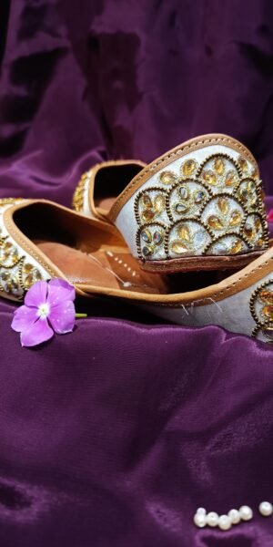 Ivory handcrafted Punjabi jutti with gold mirror work, zari embroidery, and a comfortable flat sole, ideal for bridal, festive, and traditional wear.