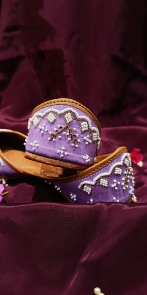 Lavender handcrafted Punjabi jutti with embroidered bird motifs, white pearl beadwork, gold zari embroidery, and a comfortable flat sole for festive and wedding wear.